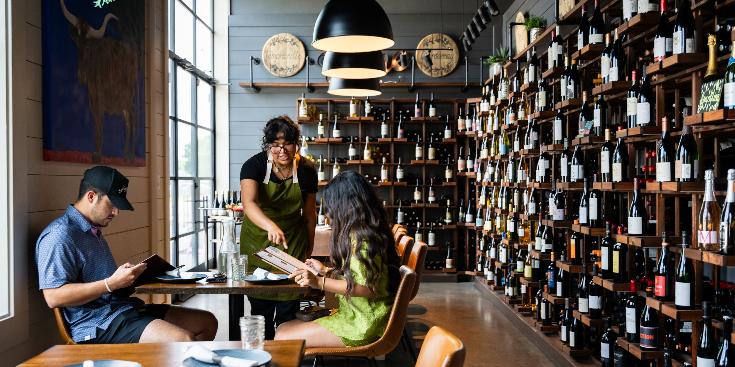 couple dining at Dos olivos with waiter and wine bottle wall